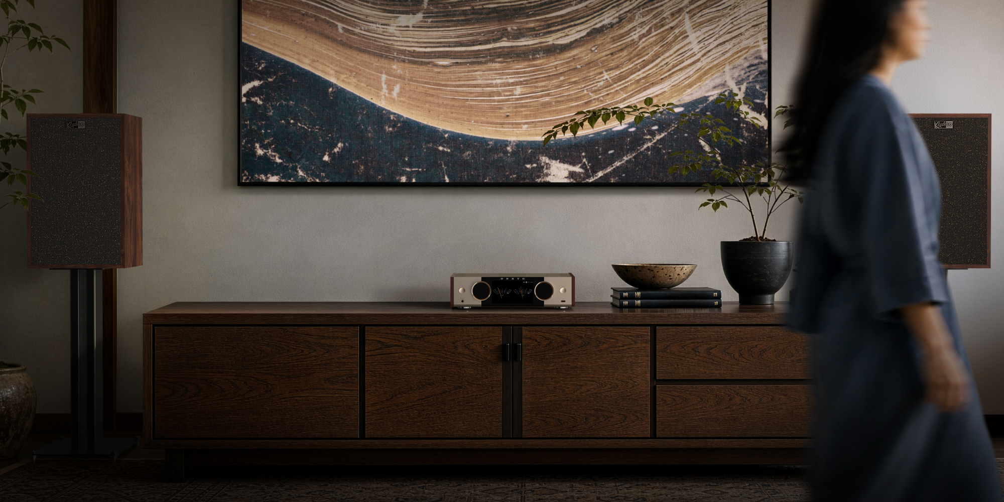 Onkyo Muse80th 01 on long media console beside speakers on stands and woman walking in blurred foreground 2000x1000