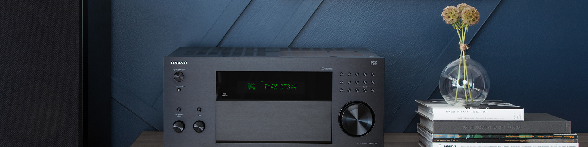 Onkyo TX RZ70 on media console beside floorstanding speakers and stack of books 2000x500