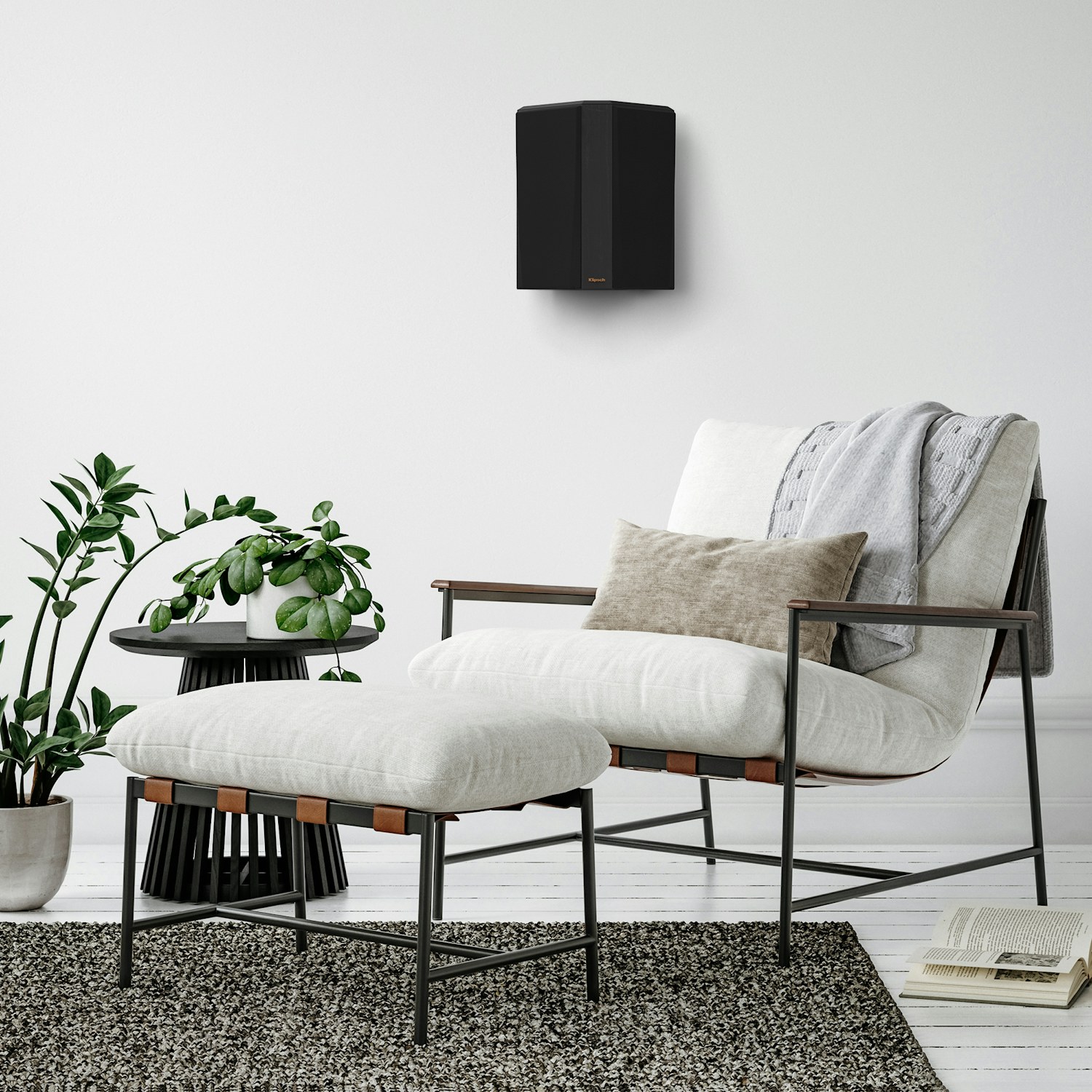 RP 502 S II surround speaker in black finish hung on a greyish wall near a chair